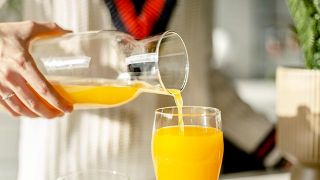 Человек наливает себе стакан апельсинового сока.