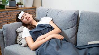 Женщина с лихорадкой лежит на диване с влажной тканью на лбу. 
